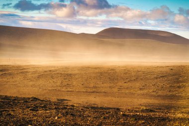 Yazın İzlanda, Landmannalaugar 'da volkanik yabanda esen güneş ışığıyla dramatik kum fırtınası manzarası.