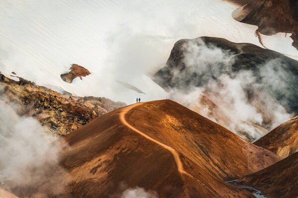 Majestic landscape of Kerlingarfjoll volcanic mountain range with sulfur smoke and tourist hiking on Hveradalir trail in summer at Highlands of Iceland
