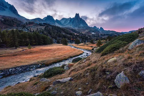 Landscape of sunset over Claree Valley with Main De Crepin peak and river flow through in larch forest during autumn at French Alps, Hautes Alpes, France