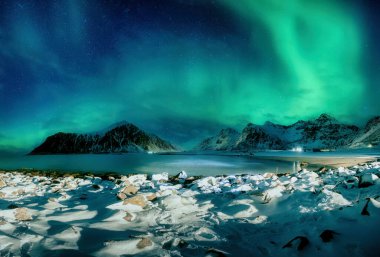 Aurora Borealis 'in fantastik manzarası, Norveç' in Lofoten Adaları 'ndaki Skagsanden Sahili' ndeki karlı dağın üzerinde parlayan kuzey ışıkları.