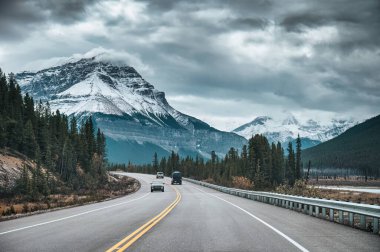 Banff Ulusal Parkı, Alberta, Kanada kasvetli ormandaki kayalık dağların arasında arabayla yolculuk
