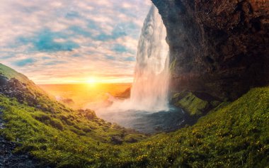 Günbatımının nefes kesen manzarası Seljalandsfoss şelalesinin içinden geçip yazın İzlanda 'ya akıyor.