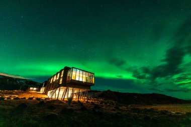 Beautiful scenic view of Aurora borealis, Northern lights glowing over luxury hotel on mount Hengill in winter at Nesjavellir, Iceland clipart