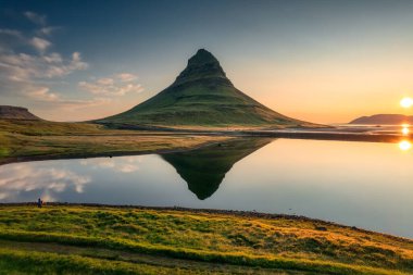 Görkemli simetri volkanı Kirkjufell 'in göl yansıması ve erkek turistin yaz sabahı İzlanda' daki Snaefellsnes yarımadasında durduğu hava manzarası.