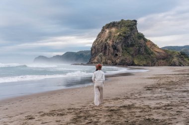 Happy young asian woman enjoying on the Piha Beach with Lion Rock at West of Auckland, New Zealand clipart