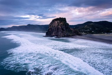 Auckland, Yeni Zelanda 'nın batı kıyısındaki Piha sahilinde güzel ikonik Aslan Kayası ve kırılan dalgaların hava manzarası.