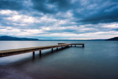 Rotorua, Yeni Zelanda 'da kasvetli bir günde bulutlu gökyüzü ile göle açılan ahşap iskele.