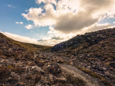 Kırsal kesimde akşam vakti gökyüzünde bulutlarla ıssız, kayalık ve çorak bir doğa manzarası.