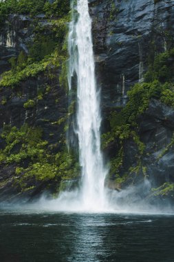 Powerful moody waterfall flowing in tropical rainforest at Milford Sound, Fjord national park, New Zealand