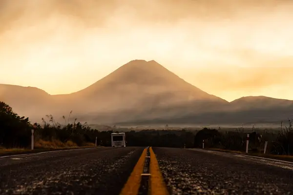 stock image Majestic volcanic Mount Ngauruhoe with golden color sky in foggy over highway road at North Island, Tongariro national park, New Zealand