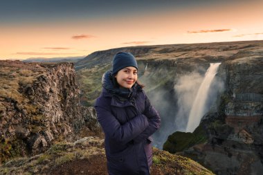 Mutlu Asyalı kadın, İzlanda 'da yaz aylarında İzlanda Dağları arasında Majestic Haifoss şelalesi ve volkanik kanyon manzarasıyla eğleniyor.