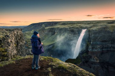 Mutlu Asyalı kadın, İzlanda 'da yaz aylarında İzlanda Dağları arasında Majestic Haifoss şelalesi ve volkanik kanyon manzarasıyla eğleniyor.