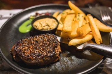 Biberli ızgara biftek, patates kızartması, masada seramik tabakta sebze.