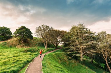 Female tourist enjoying on mountain with old growth forest and pathway in public park at the evening clipart