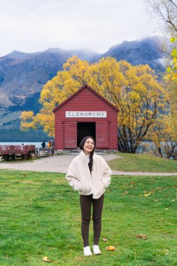 Yeni Zelanda 'nın Güney Adası, Otago' da sonbaharda Wakatipu Gölü 'nün yanında kırmızı kayıkla gezen güzel bir Asyalı kadın.
