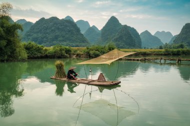 Güneşli bir günde nehirde geleneksel balıkçılık yapan balıkçı Phong Nam Vadisi, Cao Bang, Vietnam 'da dağlarla çevrili.