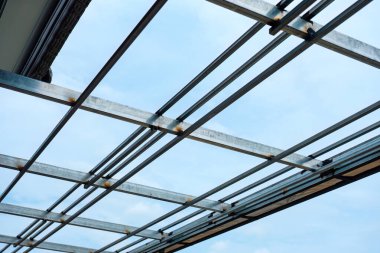 Modern çatı yapısının metal ızgara iskeleti inşaat alanındaki mavi gökyüzü arka planında tamamlanmamış