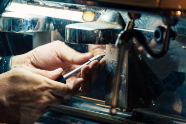 Teknisyen, kafeteryadaki tezgahta kahve makinesinden fındığı ustalıkla çıkartıyor. İçecek endüstrisinde ekipman bakımının işlem hizmeti