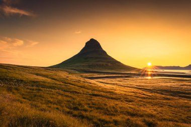 Snaefellsnes yarımadasında, İzlanda 'da Kirkjufell Dağı ve altın çayır üzerinde canlı gün doğumu parlıyor.