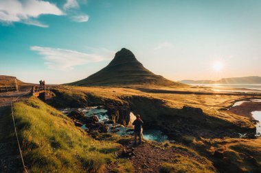 Bir fotoğrafçı Kirkjufell dağının tepesinde, sonbaharda Snaefellsnes yarımadasında Kirkjufellsfoss ile muhteşem bir gün doğumunu yakalıyor.