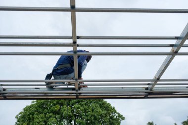 İnşaat işçisi, inşaat alanındaki inşaat alanında çelik çatı iskeletine kaynak yapıyor.