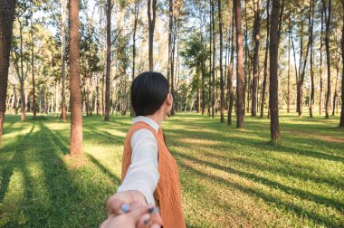 Aşığıyla el ele tutuşan kadın akşam vakti çam ormanında birlikte yürüyor.