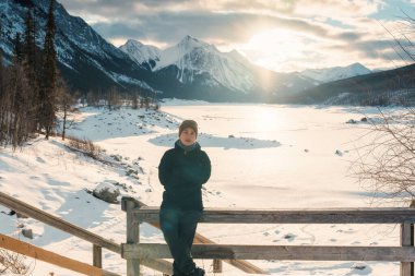 Siyah ceketli Asyalı erkek gezgin kışın Medicine Gölü 'nün üzerinde gündoğumuyla Kanada' nın Alberta kentinde Jasper Ulusal Parkı 'nda duruyor.