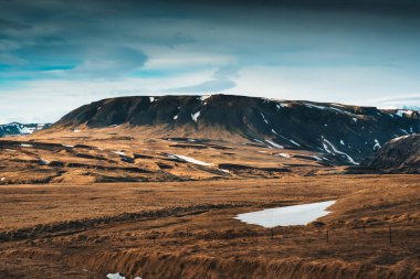 İzlanda 'da sonbahar boyunca ıssız bir yerde mavi gökyüzü olan çorak engebeli dağların manzarası.