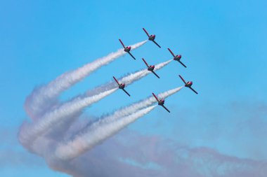 Kırmızı uçaklarla yakın bir şekilde uçan akrobatik bir takımın heyacan verici görüntüsü, parlak mavi gökyüzünde dramatik duman izleri bırakıyor. Havacılık, takım çalışması ve hava gösterisi temaları.