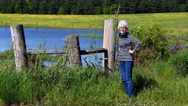 Yaşlı, taşralı bir kadın mülkünde dolaşırken duraklıyor. Üç büyük direkte bir göletin yanında çit mısırı var. İnce, çekici ve kot pantolon giyiyor..
