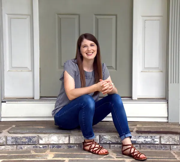 stock image Beautiful young woman sits outside her home on the front steps.  She is smiling and happy.  She has on jeans and sandals.