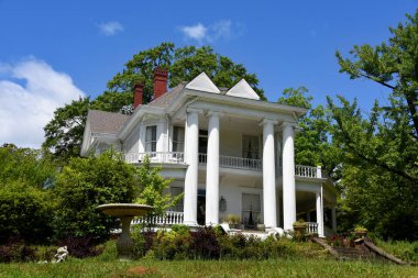 Beautiful antebellum house has four tall columns and beautiful architecture.  porch railing and yard is in need of repair and upkeep. clipart