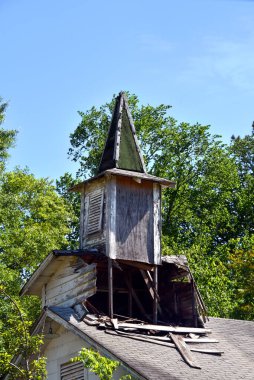 Wind damaged country church shows broken steeple.  Exposed roofline has broken boards. clipart