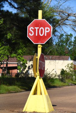 Boru tabanlı dur işareti sarı. Caddenin ortasında duruyor ve etrafından trafik geçiyor. Smackover, Arkansas 'ta yer almaktadır..