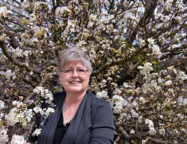 Olgun bir kadın armut ağacının dallarında poz verir. Gülümsüyor ve güneşli bir bahar gününün tadını çıkarıyor..