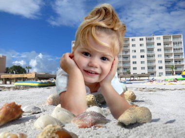 Sevimli küçük kız Florida 'daki Madeira Sahili' nde bir plaj tatili hayal ediyor. Deniz kabuğu avlamayı çok seviyor. Konut arka planda görülebilir ve çocuk deniz kabuklarının üzerinde yatar.                        