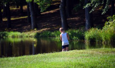 Genç çocuk Ak Meşe Gölü kıyısında balık tutuyor. Yaz zamanı ona şort ve kolsuz tişört giydirir. Bir çubuk tutuyor ve bir ısırık için bekliyor..