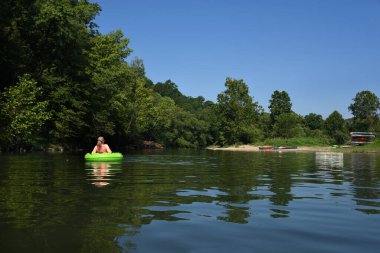 Kadın nazikçe Caddo Nehri 'ni yüzdürüyor, Glenwood, Arkansas. Limon yeşili bir ara borunun içinde ve az önce giriş sahili terk etti. Yüzücüler için diğer yüzme cihazları hazır..
