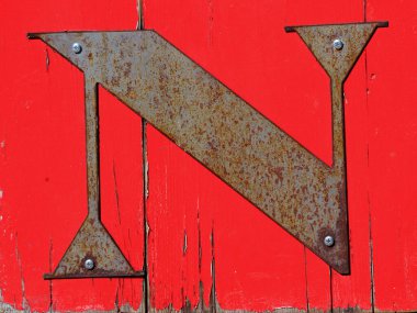 N harfi metalden yapılmıştır ve vidalarla kırmızı tahtaya tutturulmuştur. N paslanmaya başladı, ve ahşap çatlamış ve pürüzlü..