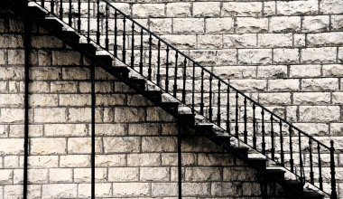 Sanatsal görüntü siyah, dövülmüş demir merdiveni gösteriyor. Eski tarihi taş bina üzerinde çaprazlama yükseliyor..