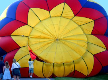 Hot Air Balloon expands and inflates as it is prepared for its flight during Hot Air Balloon Festival in Kingsport, Tennessee.  Bystanders watch as worker prepares it. clipart