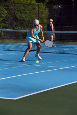 Senior female reaches to return a pickle ball during a game in Asheville, North Carolina.  She is wearing a turquoise tennis outfit. clipart