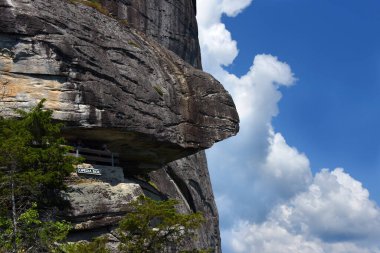 Visitors pause at the Opera Box view point, at Chimney Rock State Park, North Carolina.  Rocky bluff hangs over trail. clipart