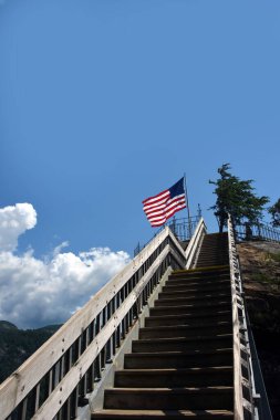 Wooden steps lead to viewing platform at top of Chimney Rock at Chimney Rock State Park, North Carolina.  American flag flies on platform. clipart