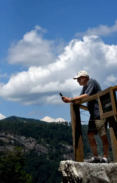 stock image Elderly man uses his phone to snap a photo of Hickory Nut Falls.  He is leaning on the rail of the viewing platform.