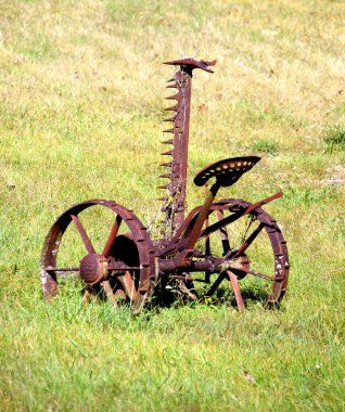 Eski çim biçme makinesi. Koltuğu var, tarlada paslanıyor. Çim biçme bıçağı dik duruyor.. 