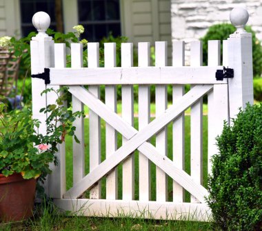 Evin önünde siyah donanımlı beyaz ahşap bir kapı var. Yuvarlak top filikaları her uçtaki direğin üstünde.