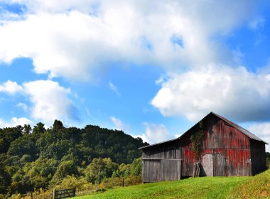 Kırmızı ahşap ahır Tennessee 'deki Appalachian Dağları' nın yamacına tutunur. Mavi gökyüzünde kabarık beyaz bulutlar var.