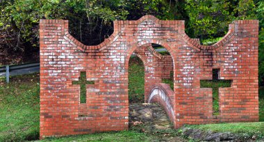 Brick bridge has castle style front wall with crosses shaped into the structure.  Arched bridge has stone surface and brick sides. clipart