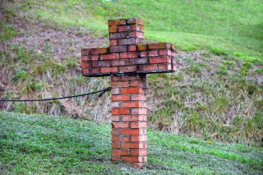 Brick shaped cross has rope attached to its side.  Brick is red and orange. clipart